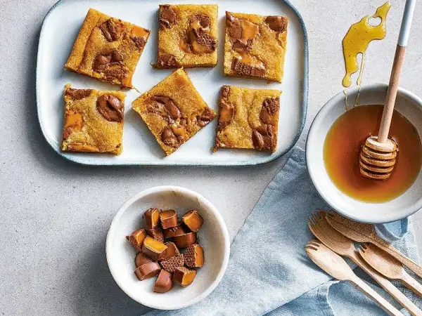 Enkla dumlekakor med chokladbitar på en bricka, bredvid en skål med honung och en skål med hackade dumlekolor.