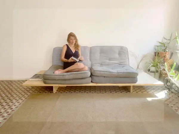 Frau liest auf einem selbstgebauten Sofabett mit grauen Polstern und Holzrahmen.