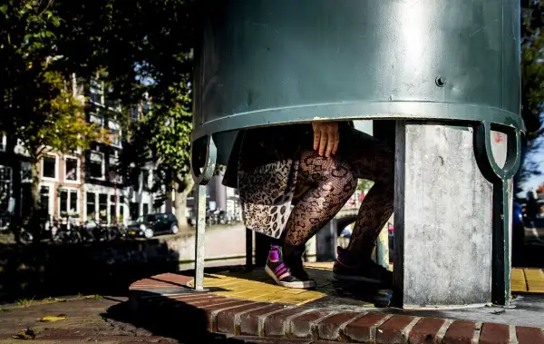 Een plassende vrouw in een urinoir, met opvallende panty's en sneakers.