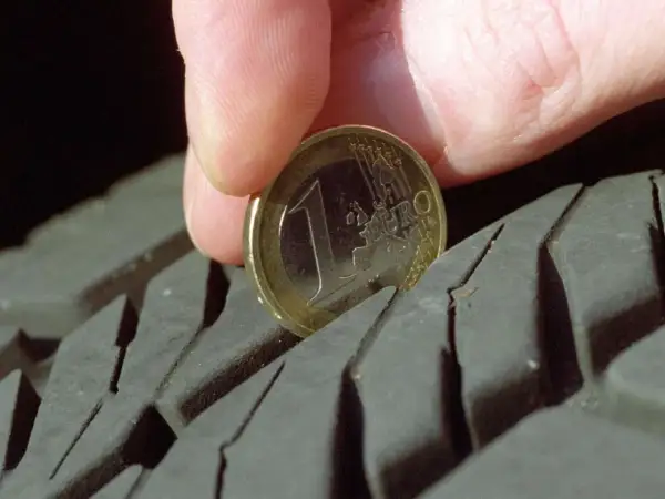 Daumen und 1-Euro-Münze messen Reifenprofiltiefe.