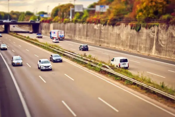 Voitures et camion circulent sur l'autoroute A85, sous un pont, avec des arbres aux couleurs d'automne sur les talus.