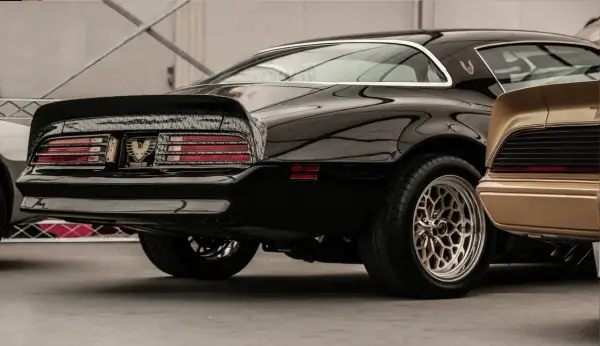 Błyszczący czarny muscle car z charakterystycznym spojlerem i felgami. Obok złoty klasyk.