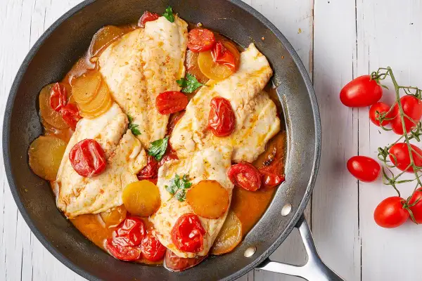 Orata in padella con pomodorini e patate, un piatto succulento e colorato, pronto per essere gustato.