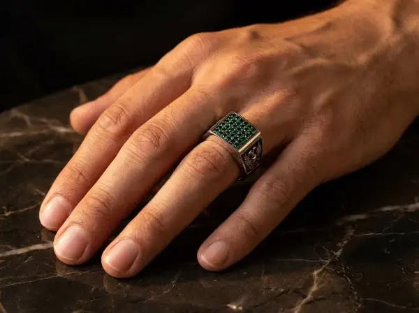Anillo de plata con piedras verdes, puesto en el dedo anular, el dedo en que se pone un anillo normal.
