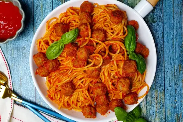 Un piatto invitante di spaghetti con polpette, conditi con salsa rossa e guarniti con foglie di basilico fresco.