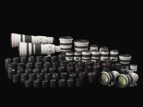 Vasta collezione di obiettivi per fotocamere, con diversi modelli e marche di macchine fotografiche, disposti su sfondo nero.