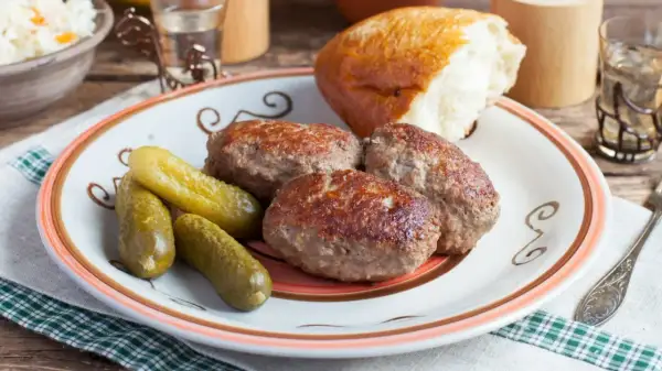 Kotlety mielone z pieczarkami, ogórki kiszone i bułka na talerzu. Pyszny, domowy obiad.