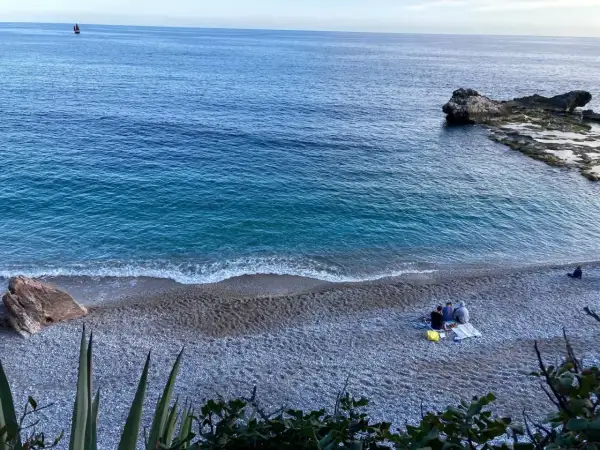 Un mare bello nel nord Italia, con un veliero all'orizzonte e persone che si godono la spiaggia di ciottoli.