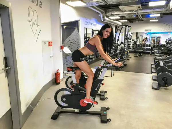 Kobieta na rowerze stacjonarnym w siłowni. Czy trening siłowy czy cardio na odchudzanie? Ona wybrała cardio!