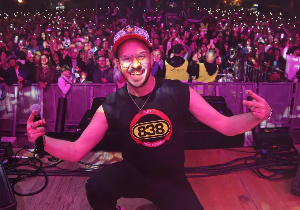 Max Pezzali sul palco, con la folla illuminata dai cellulari, indossa una maglietta con il logo 883.