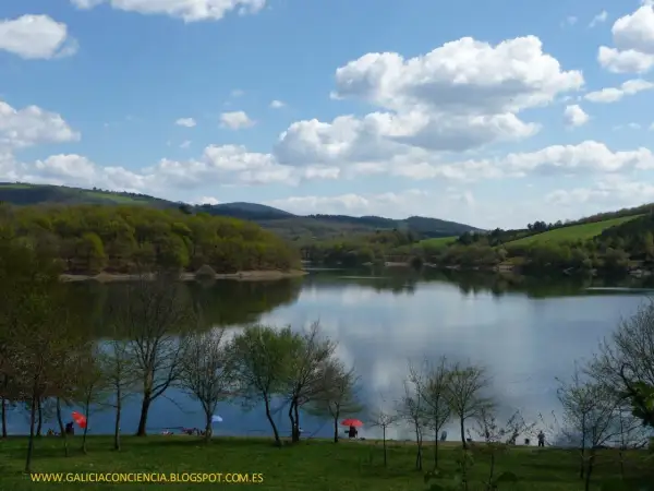 El embalse de Vilasouto, con sus aguas serenas reflejando el cielo azul y las verdes colinas, invita a disfrutar de un día tranquilo.