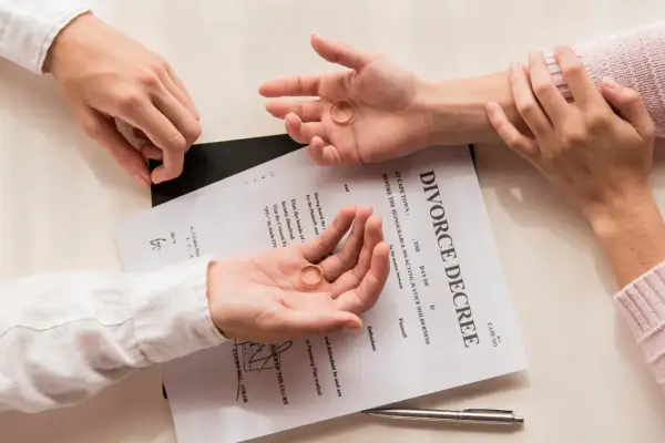Dwie dłonie trzymają obrączki na tle dokumentu "DIVORCE DECREE". Zastanawiasz się, jak napisać papiery rozwodowe?
