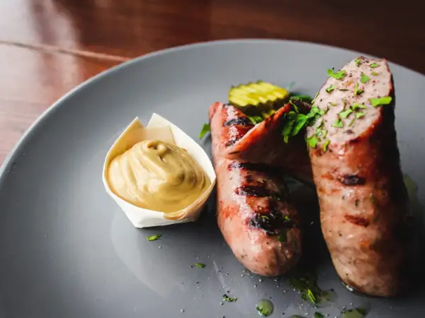 Zwei saftige, gegrillte Bratwürste mit Senf und Gurkenscheiben. Frische Bratwurst wie lange haltbar? Am besten sofort genießen!