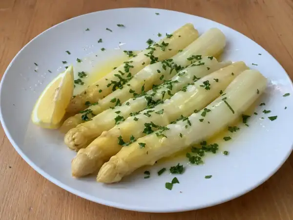 Välkokt vit sparris serverad på en vit tallrik med smält smör, hackad persilja och en citronklyfta. Enkel och god rätt!