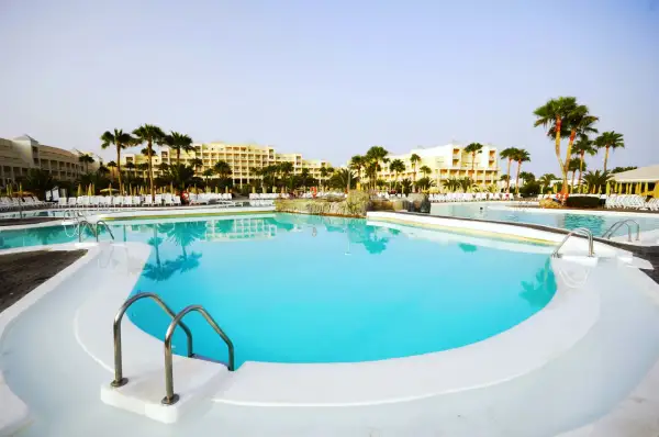 Piscina con acqua cristallina e palme, ideale per una vacanza rilassante. La **clorocaucciù scheda tecnica** descrive i materiali resistenti usati.