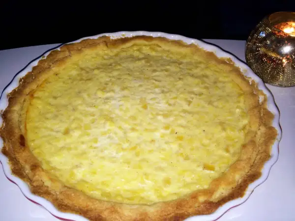 En gyllene ananaspaj glutenfri med en krämig fyllning. En ljuslykta glimmar i bakgrunden.