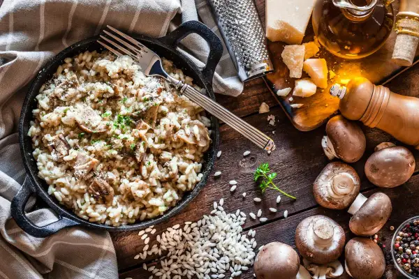 Un cremoso risotto de setas servido en sartén de hierro fundido, con champiñones frescos, arroz, queso parmesano y perejil picado.