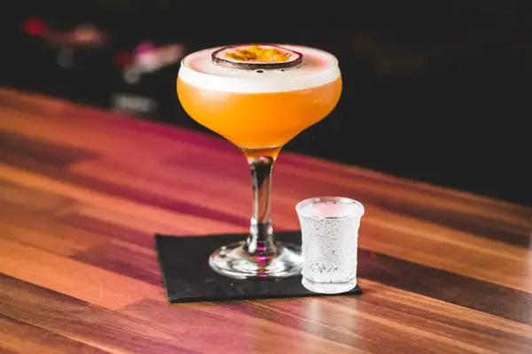 Pomarańczowy koktajl Pornstar Martini z owocem marakui i kieliszek szampana. Idealny sposób, by zacząć wieczór.