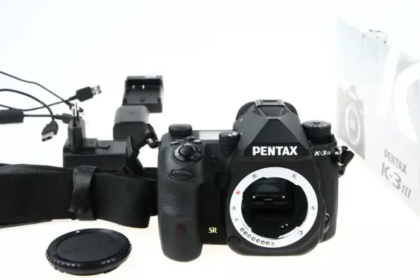 Czarny aparat Pentax K-3 III, ładowarka i akcesoria. Czy to lustrzanka czy bezlusterkowiec? To lustrzanka.