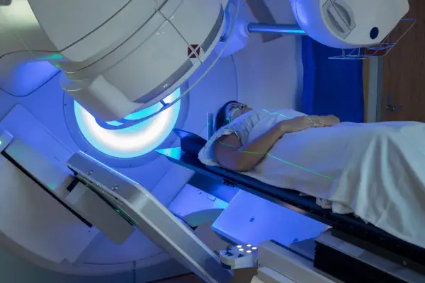 Frau liegt auf Liege unter Bestrahlungsgerät. Grüne Laserlinien markieren die Position. Strahlentherapie Brustkrebs Erfahrungen.