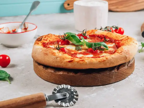 Pyszna pizza na drewnianej desce, gotowa do pokrojenia. Idealna do piekarnika, dzięki kamieniowi do pizzy.