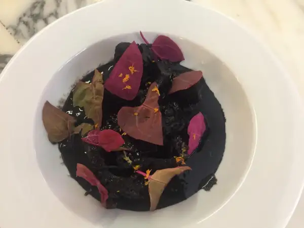 Un plat de ragout de seiche à l'encre noire, garni de pétales de fleurs séchées et d'une touche d'agrume.