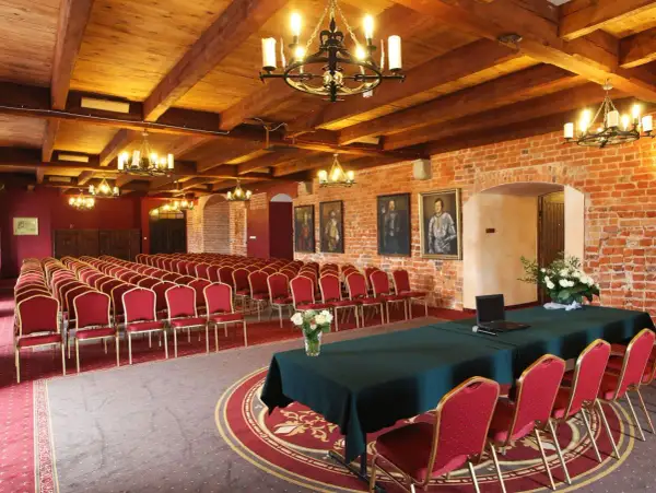 Elegancka sala konferencyjna w hotelu z **luxury collection**, z rzędami czerwonych krzeseł, drewnianym sufitem i ceglanymi ścianami.