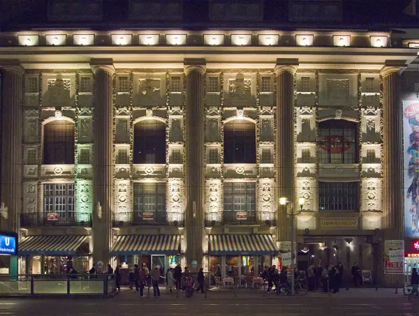 Der Admiralspalast Berlin bei Nacht, beleuchtet mit Säulen und Verzierungen. Menschen stehen vor den Eingängen und Cafés.