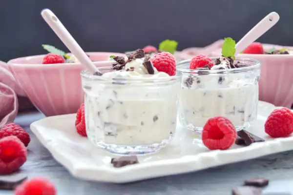 Zwei Gläser mit cremigem Dessert, garniert mit Himbeeren und Schokostückchen. Ein leckeres Herrencreme Rezept zum Nachmachen.