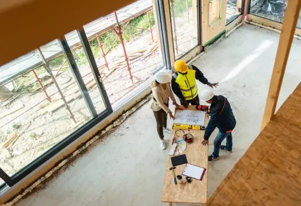 Architekci omawiają projekt, ustalając, ile kosztuje strop drewniany. Na stole plany, narzędzia i próbki materiałów.