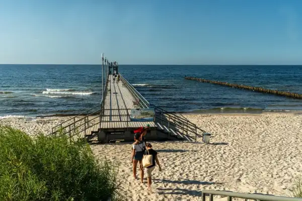 Sianożęty atrakcje: drewniane molo na plaży, ludzie spacerują, morze i niebo.