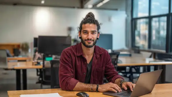 Junger Mann mit Dutt am Laptop, lächelnd. Ein zukünftiger marketing master hamburg.
