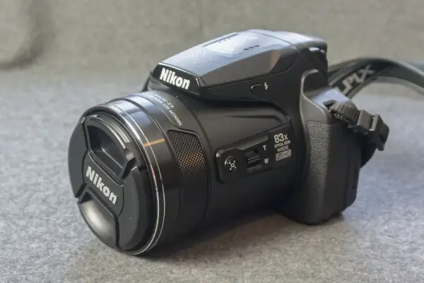 A black Nikon P90 camera with an 83x optical zoom lens sits on a textured gray surface.