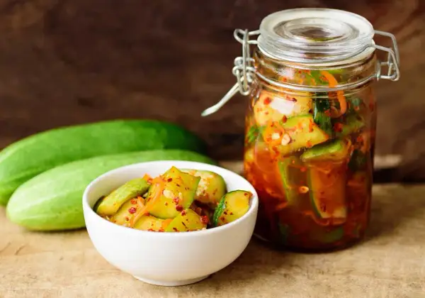 Słoik i miseczka z pikantnymi ogórkami z papryką chili, obok świeże ogórki.