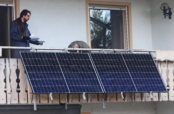 Dos hombres instalan placas solares en una terraza. Uno revisa un papel mientras el otro se inclina sobre los paneles.