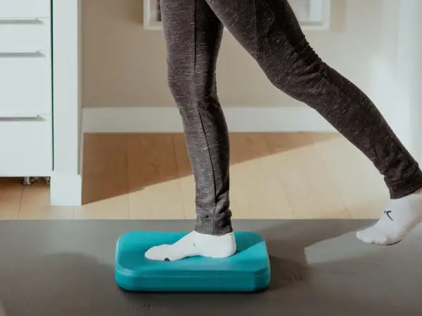 Exercice d'équilibre sur un coussin bleu pour améliorer la proprioception cheville.