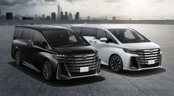 Dwa luksusowe minivany Toyota Vellfire, czarny i biały, prezentują się na tle miejskiej panoramy.