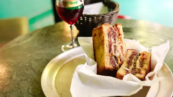 Un delicioso patty melt con carne jugosa y cebolla caramelizada, servido en pan tostado, junto a una copa de vino tinto.
