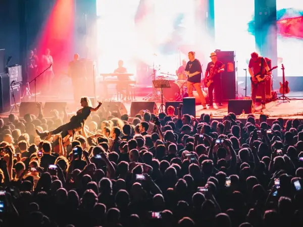 Energiczny koncert w klubie Stodoła Warszawa. Tłum szaleje, a na scenie gra zespół. Jedna z fanek jest niesiona przez publiczność.