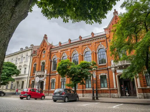 Kamienice w Radomiu, w tym Bank Polski, to ciekawe atrakcje miasta. Dwa samochody zaparkowane na brukowanej ulicy.