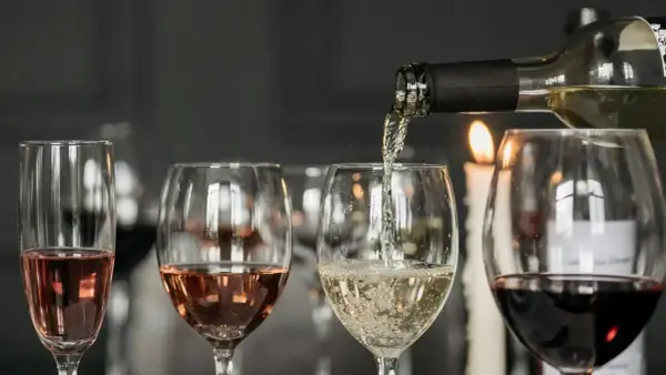 Degustacja wina w blasku świec. Nalewanie białego wina do kieliszka, obok różowe i czerwone wino.