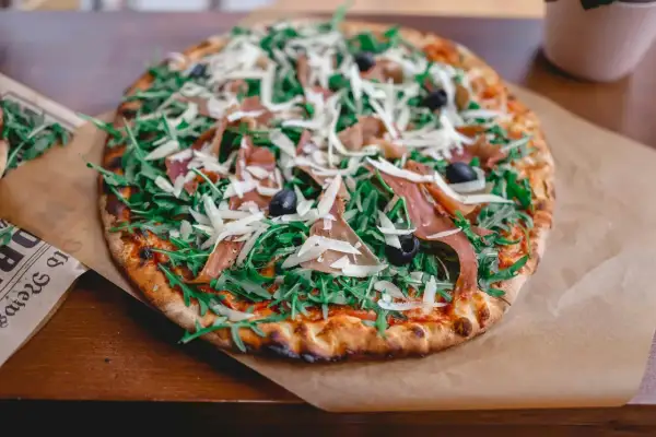 Pizza z rukolą, szynką parmeńską i oliwkami, posypana obficie startym parmezanem do pizzy.
