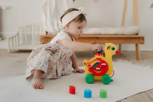 Mała dziewczynka w kwiecistej sukience bawi się żółtym pajacykiem zabawką na kółkach.