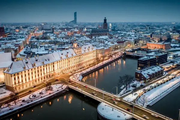 Zimowy Wrocław nocą. Ośnieżone dachy, rzeka i mosty tworzą magiczny widok. Warto odkrywać wrocławskie atrakcje zimą.