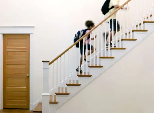 Two people with backpacks ascend a staircase with a new white stair railing and wooden handrail.