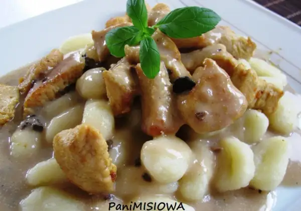 Pyszne gnocchi z kurczakiem w sosie śmietanowym, udekorowane listkiem bazylii. Danie wygląda apetycznie i sycąco.