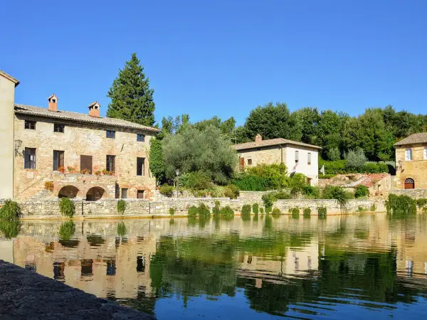 Antica sorgente termale con edifici in pietra e riflessi sull'acqua, un incantevole scorcio dei borghi del Val d'Orcia.