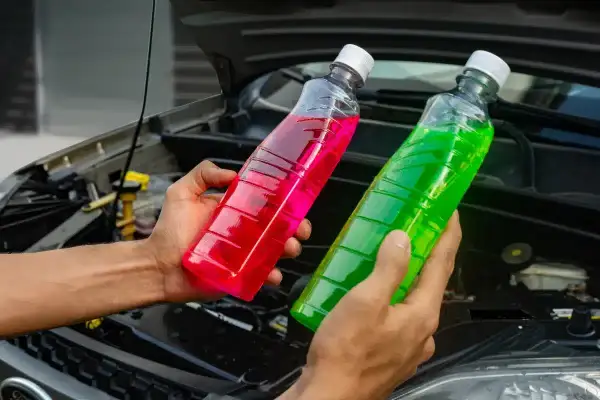 Deux mains tiennent des bouteilles de liquide de refroidissement coloré, rose et vert. Quel liquide de refroidissement choisir pour votre voiture ?