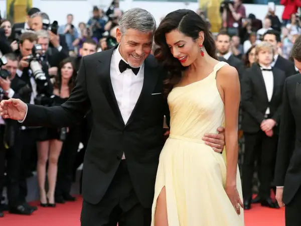 George und Amal Clooney auf dem roten Teppich, ein Beispiel für den Gala-Dinner-Dresscode: Er im Smoking, sie in einem eleganten gelben Kleid.