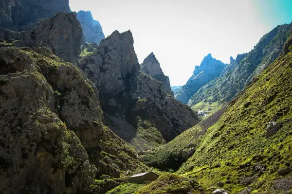 Kamienna chata w dolinie u stóp skalistych szczytów, przypominających kształtem **Naranjo de Bulnes**.